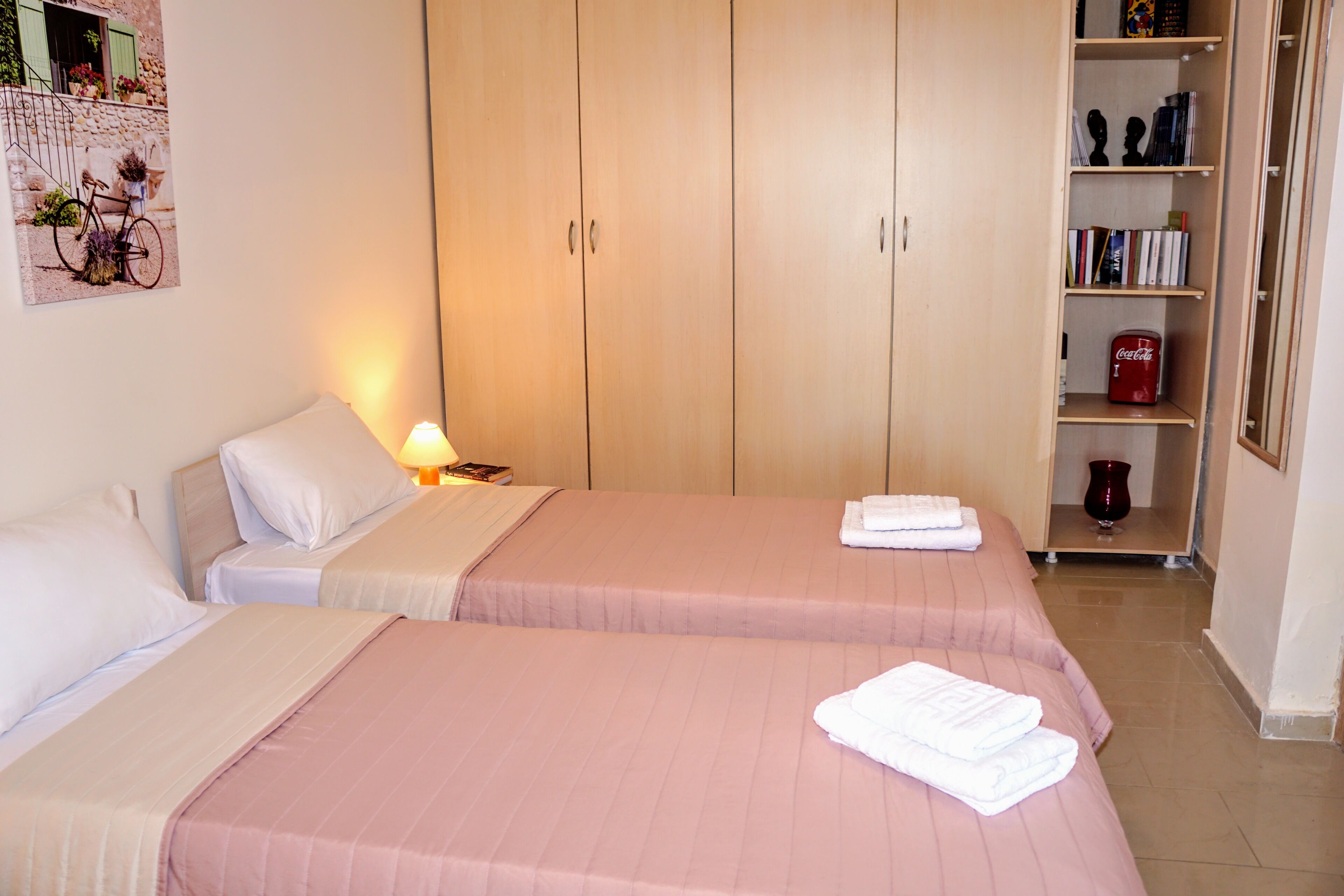 A hotel room with two beds, a bookshelf, and a framed picture on the wall.