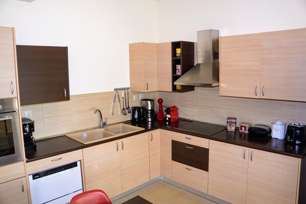 A compact kitchen with wooden cabinets, a stainless steel sink, and modern appliances including a dishwasher and coffee maker. - Olive Tree Hillside Apartment (Chania)