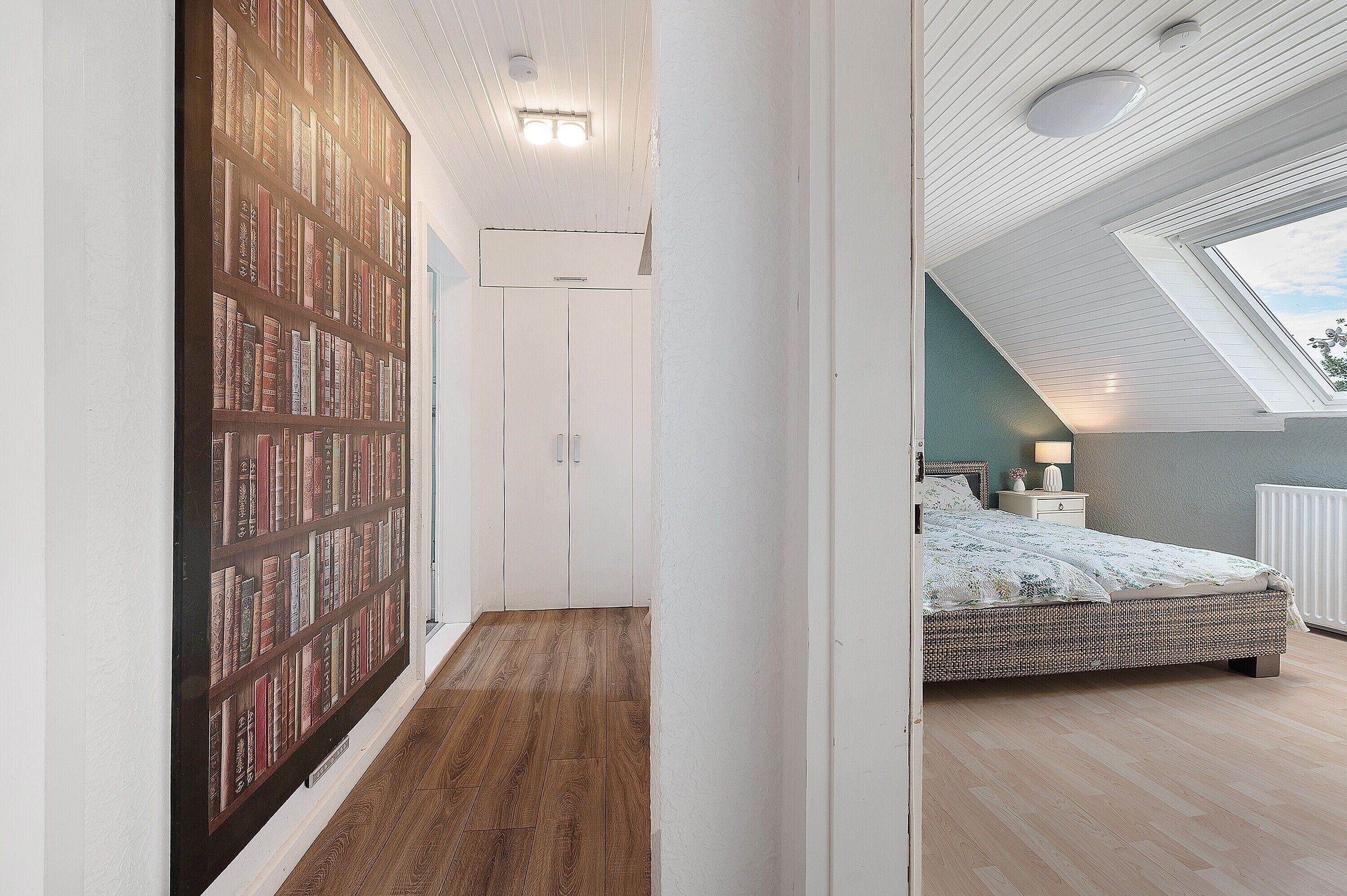 Ein Schlafzimmer mit Dachfenster, einem Bücherregal und einem Bett mit gemustertem Überwurf.