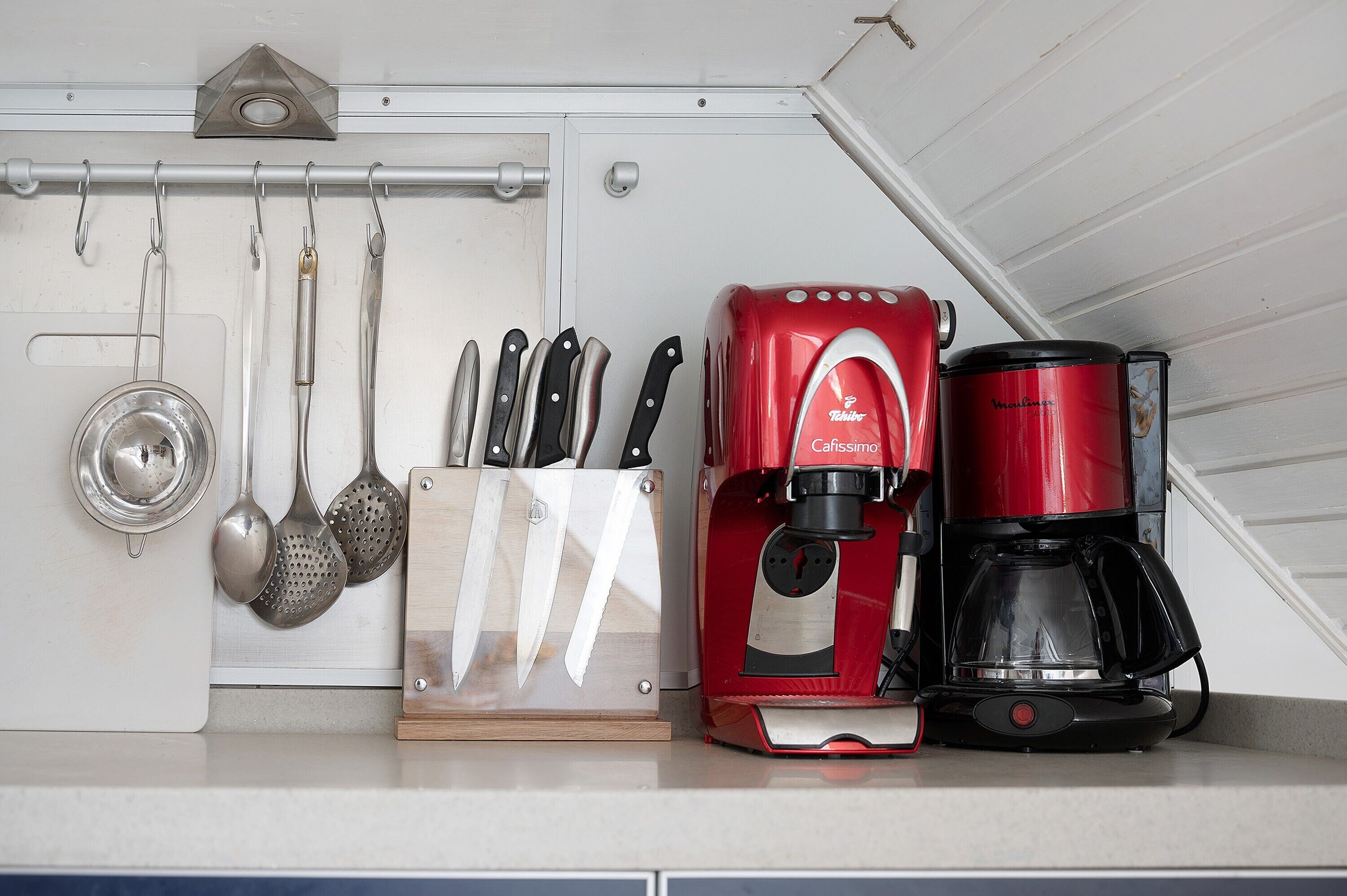 Een keuken met een koffiezetapparaat, een messenblok en hangend keukengerei.