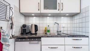 A modern kitchen with white cabinets, a granite countertop, a coffee maker, a kettle, and a dish rack.