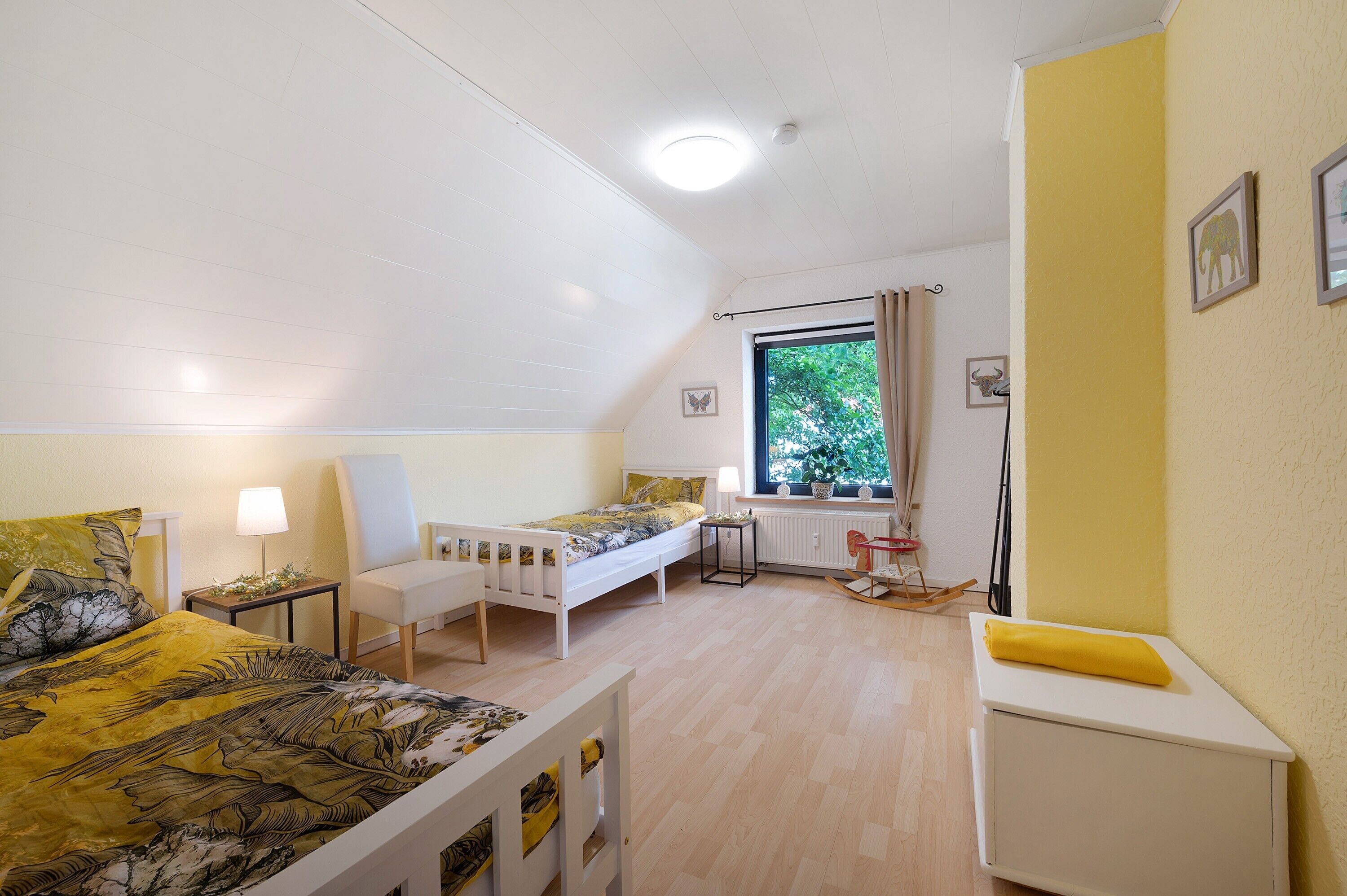 Quarto com duas camas, janela, radiador e uma mesinha.