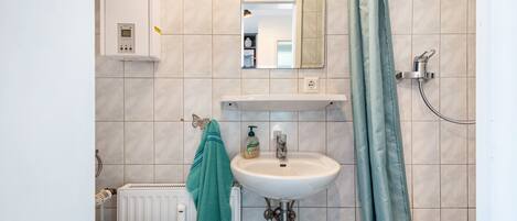 Une salle de bain avec un lavabo blanc, un miroir, une douche et un porte-serviettes.