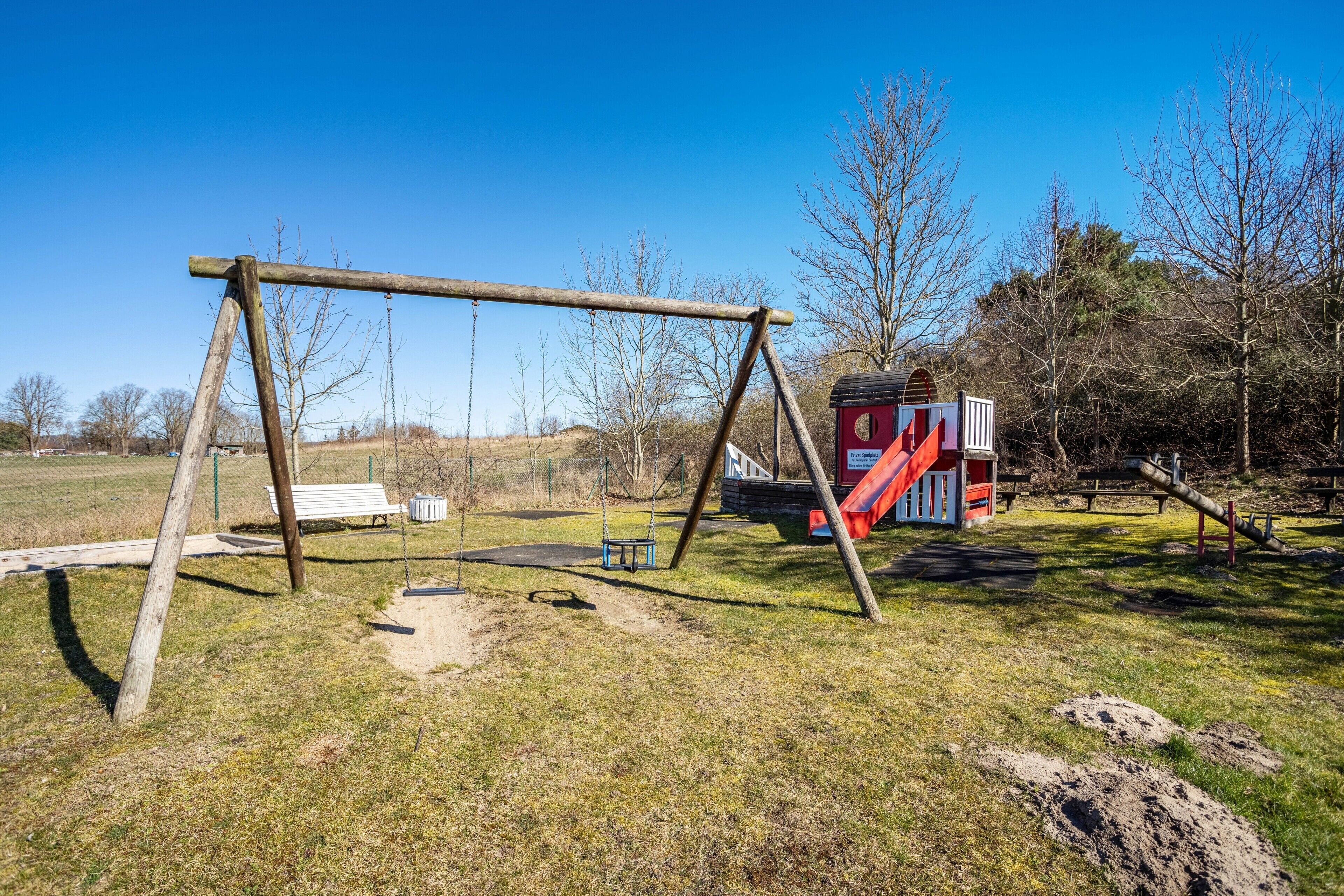 A playground with a swing set, a slide, and a small red building.