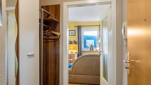 Un couloir mène à une chambre qui contient un lit, une armoire en bois et une fenêtre avec des rideaux.