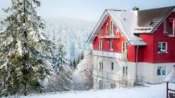 Un bâtiment rouge et blanc à deux étages, doté d’un balcon, entouré d’arbres couverts de neige et adossé à une forêt.