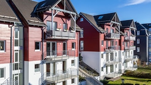 Une rangée d’immeubles d’appartements aux façades rouges et blanches, dotés de balcons, un ciel dégagé et une pelouse bien entretenue.