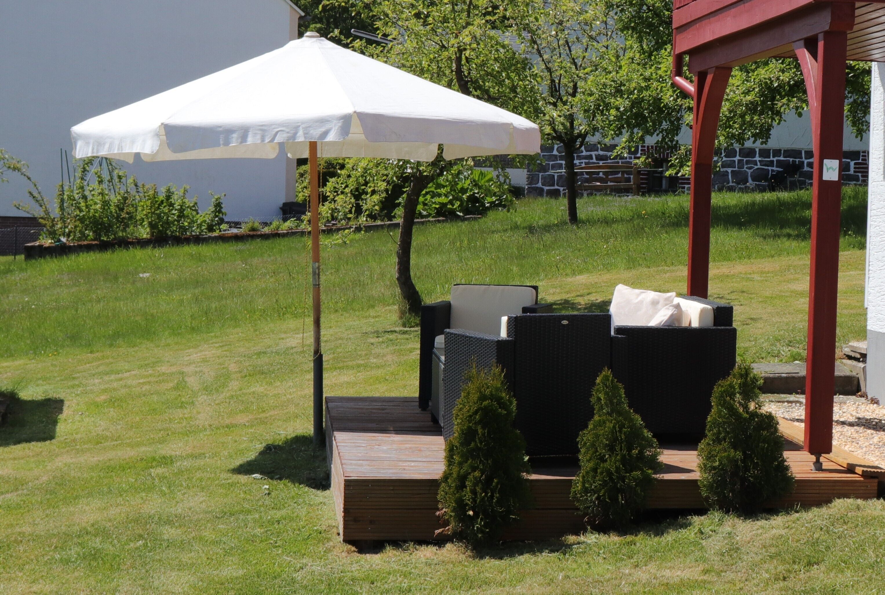 A patio with outdoor furniture, a white umbrella, and small potted plants.