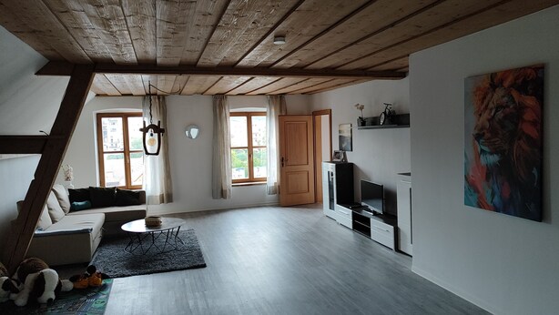 En rummelig loftetage med højt til loftet, træbjælker, en sofa, et fjernsyn og et maleri.