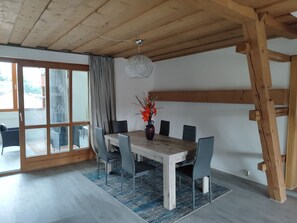 A dining area with a wooden table, chairs, a vase with flowers, and a view through a glass door. - Bruckmühle Vacation Apartment, 2 bedrooms, ideal for families. (Wasserburg am Inn)