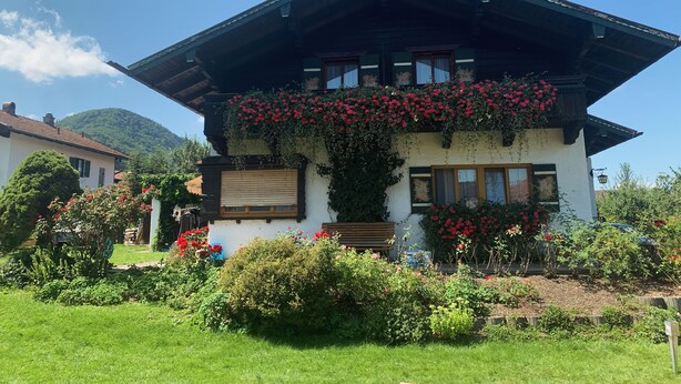 A traditional chalet with a sloped roof, wooden shutters, and a balcony adorned with red flowers. - Vacation apartment Wolke 7 (Rottau)