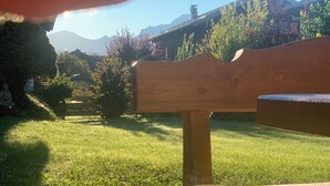A wooden bench with a white mug featuring a heart design, set on a table in a grassy outdoor area with a mountain backdrop. - Vacation apartment Wolke 7 (Rottau)