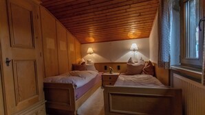 A room with two single beds, wooden walls, a sloped ceiling, and two wall-mounted lamps. - Vacation apartment Wolke 7 (Rottau)