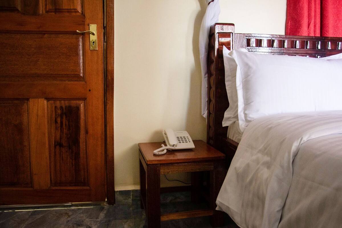 Eine Holztür, ein Nachttisch mit einem weißen Telefon und ein Bett mit weißer Bettwäsche.