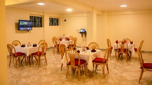 A dining area with multiple tables and chairs, a television mounted on the wall, and a laptop on a stand. - Turbine Ngong Hotel (Ngong)