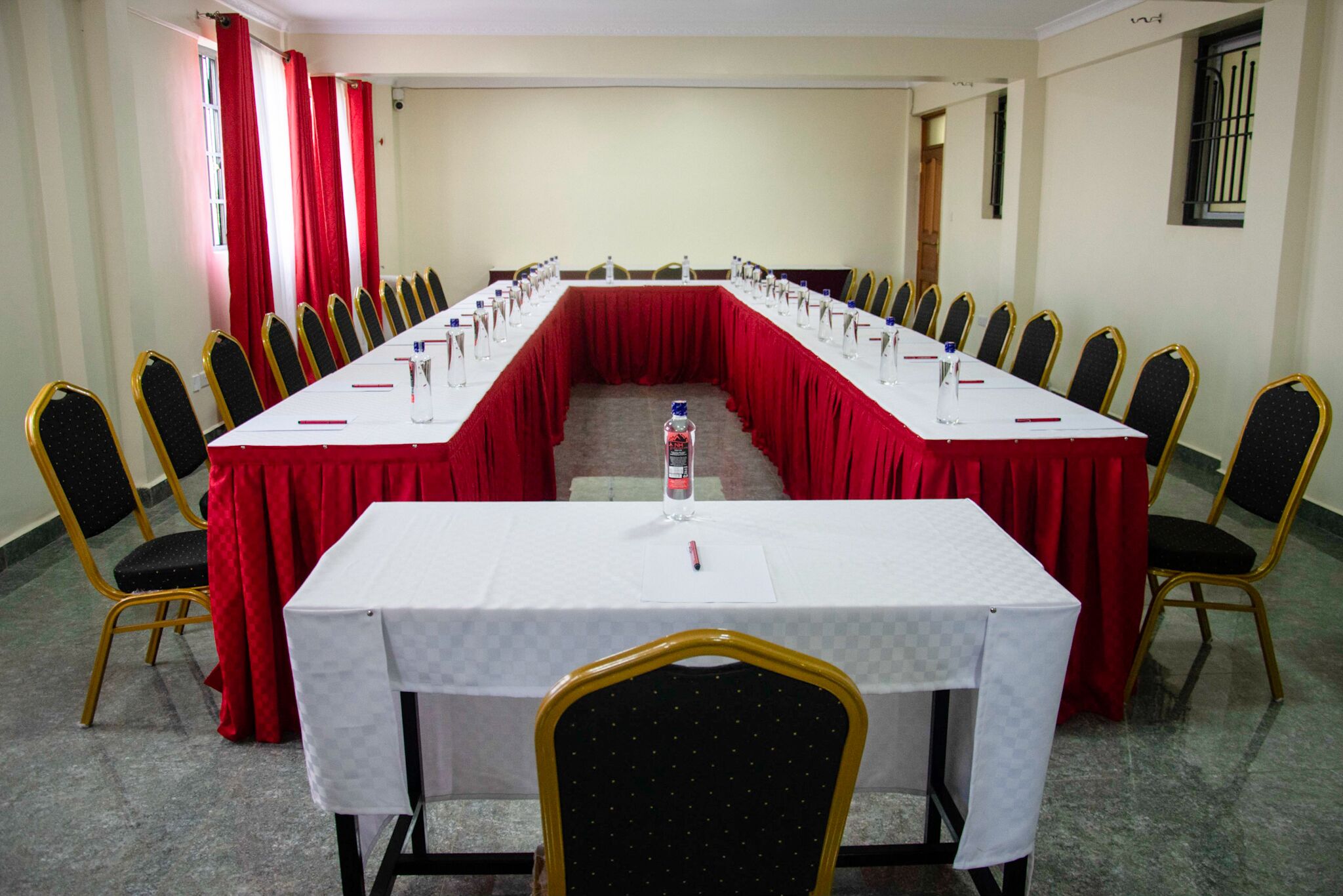 Une salle de conférence avec une longue table, des nappes rouges et des rangées de chaises.