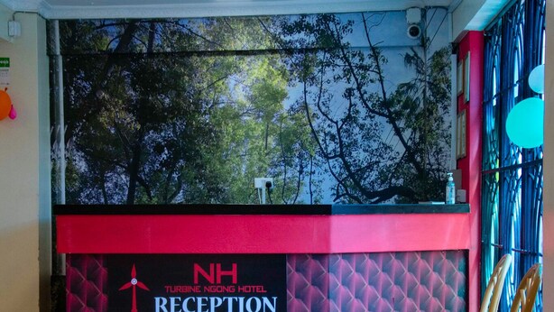 A reception area with a red and black color scheme, a sign for NH Turbine Ngong Hotel Reception, and a view of trees through the window. - Turbine Ngong Hotel (Ngong)