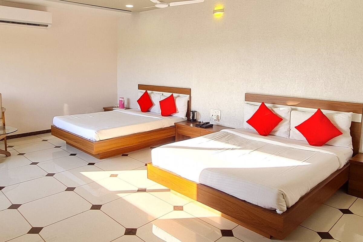 A hotel room with two beds, a chair, a table, and an air conditioning unit.
