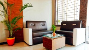 A modern waiting area with a black leather sofa, a glass-top coffee table, and a red potted plant. - HOTEL SHIV SHAKTI (Goharganj)