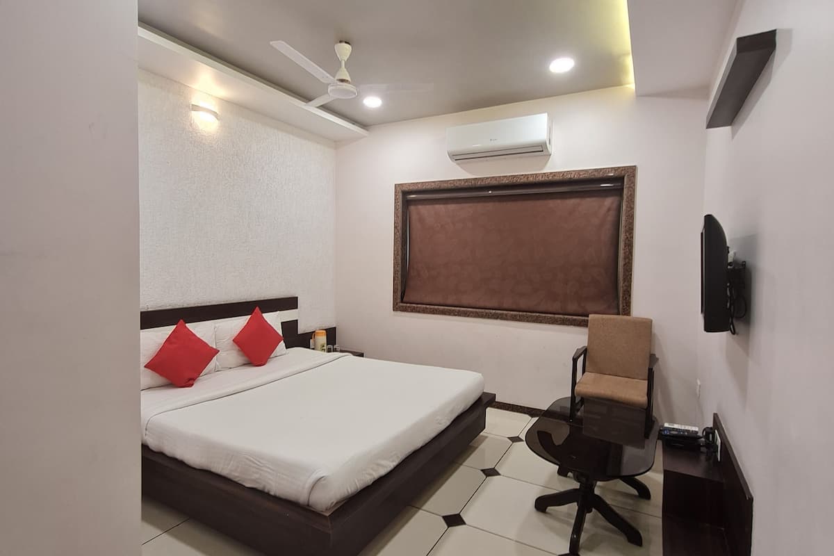 A modern bedroom with a large bed, a desk, a chair, an air conditioning unit, and a ceiling fan.