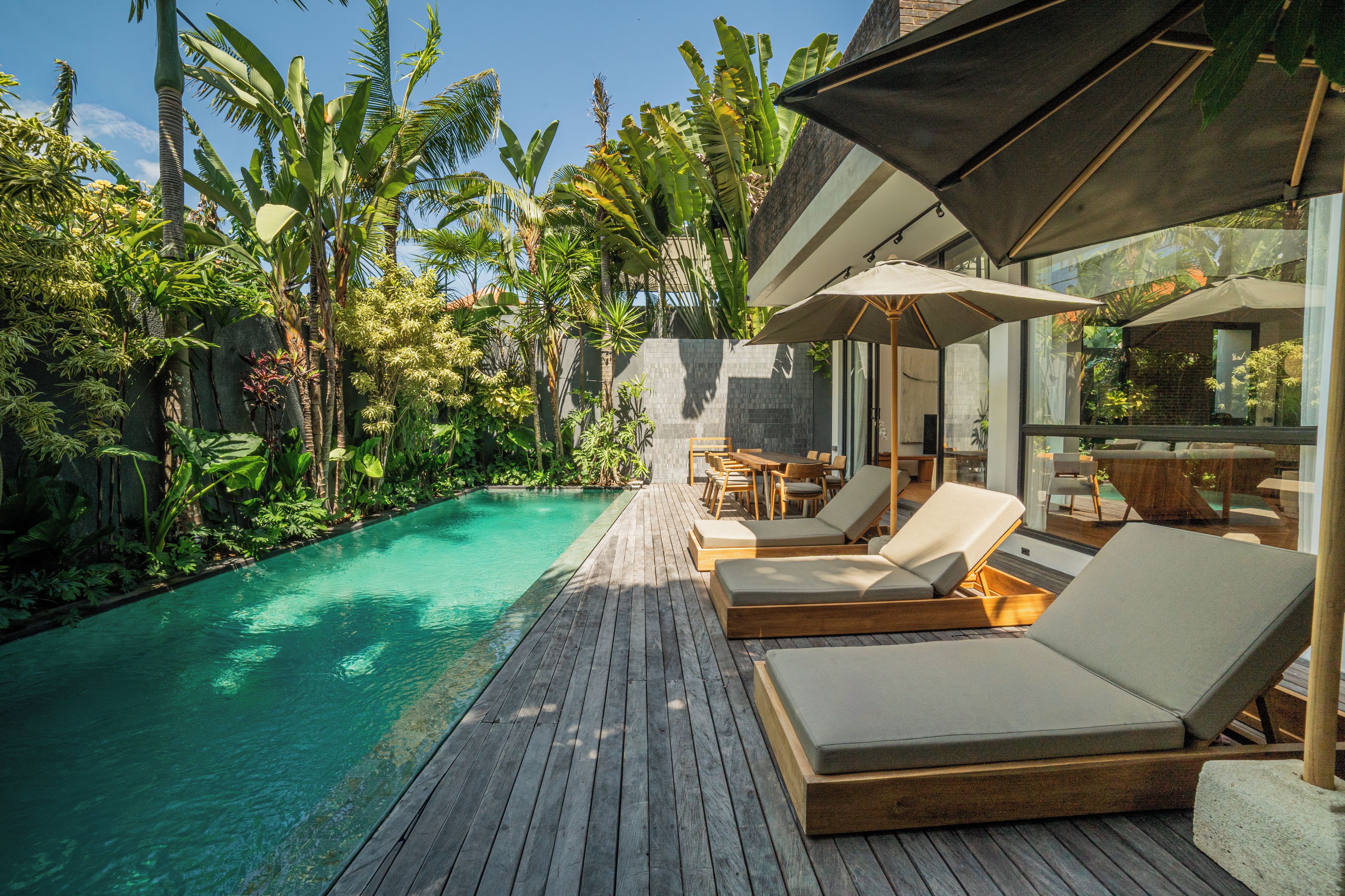 A wooden deck with lounge chairs and a pool, surrounded by tropical plants.