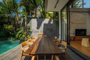 A wooden deck with a pool, surrounded by tropical plants and a stone wall.