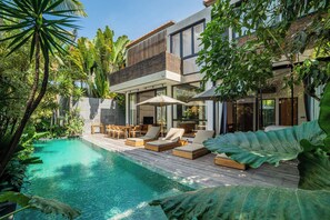 A modern house with a pool, outdoor furniture, and lush greenery.