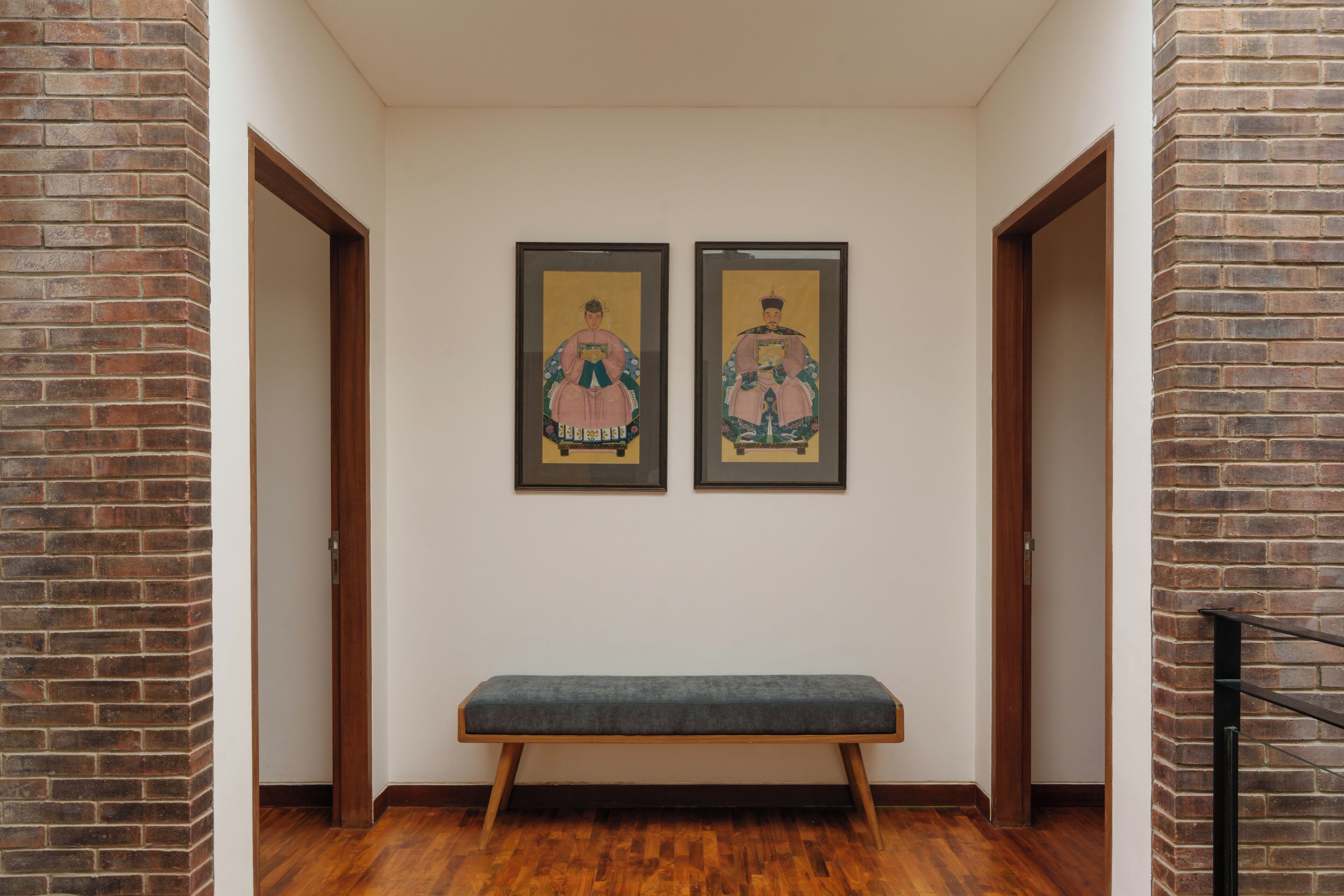 A hallway with a bench, two framed artworks on the wall, and wooden doors.