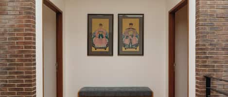 A hallway with a bench, two framed artworks on the wall, and wooden doors.