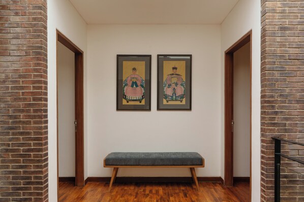 A hallway with a bench, two framed artworks on the wall, and wooden doors.