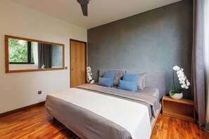 A modern bedroom with a large bed, a mirror, and a view of greenery outside.