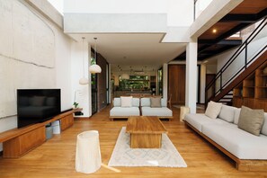 Una sala de estar moderna con televisor de pantalla plana, sofás, una mesa de centro y una escalera.