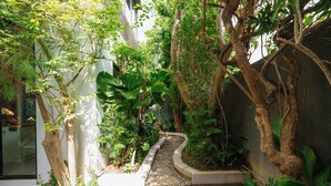 A narrow pathway flanked by lush greenery and a white wall, leading to a building entrance. - Villa Pakuk by Alfred in Bali (Canggu)