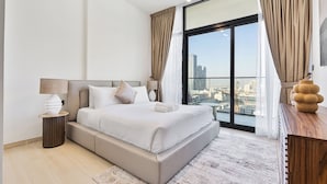 Un dormitorio moderno con una cama grande, una mesita de noche, una lámpara y vistas a la ciudad a través de un ventanal.
