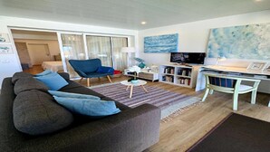 Un salon avec un canapé gris, un fauteuil bleu, une petite table ronde et une bibliothèque.