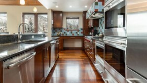 A modern kitchen with wooden cabinets, stainless steel appliances, and a large window overlooking a snowy landscape. - Cascade Village - Westhaven Condo Sleeps 24 (Vail)