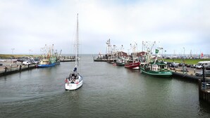 Ein Hafen mit mehreren vertäuten Booten, ein Segelboot im Vordergrund und ein Leuchtturm im Hintergrund.
