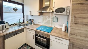 Eine kleine Küche mit weißen Schränken, einer Edelstahl-Dunstabzugshaube, einem Backofen und einer Mikrowelle.