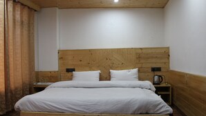A wooden bed with white bedding in a room with wooden walls and a sloped ceiling. - Apple Field House - Hotel in Old Manali (Manali)