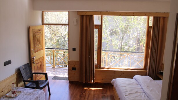 A room with a bed, a chair, a small table, and a window with curtains. - Apple Field House - Hotel in Old Manali (Manali)