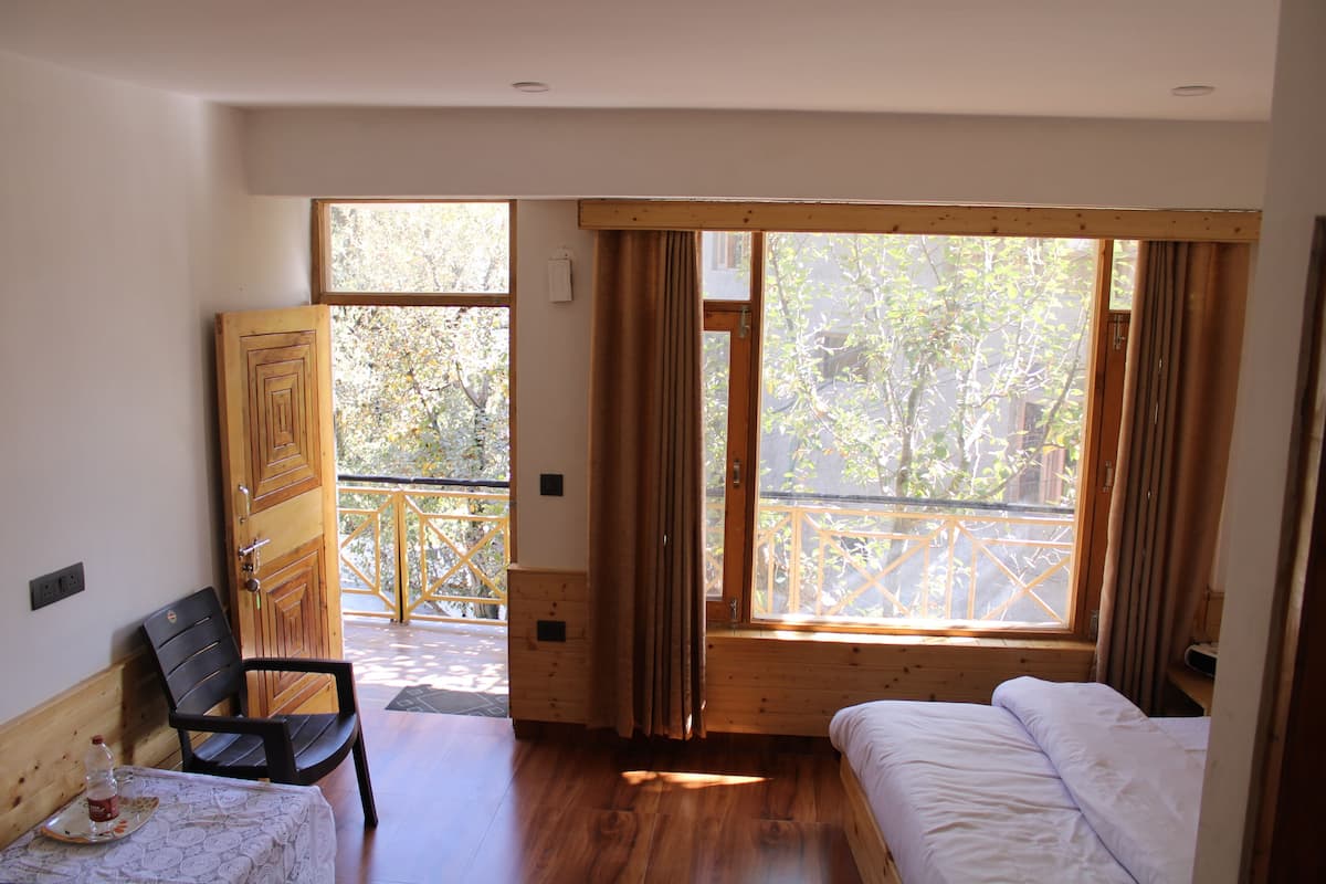Una habitación con cama, una silla, una mesita y una ventana con cortinas.