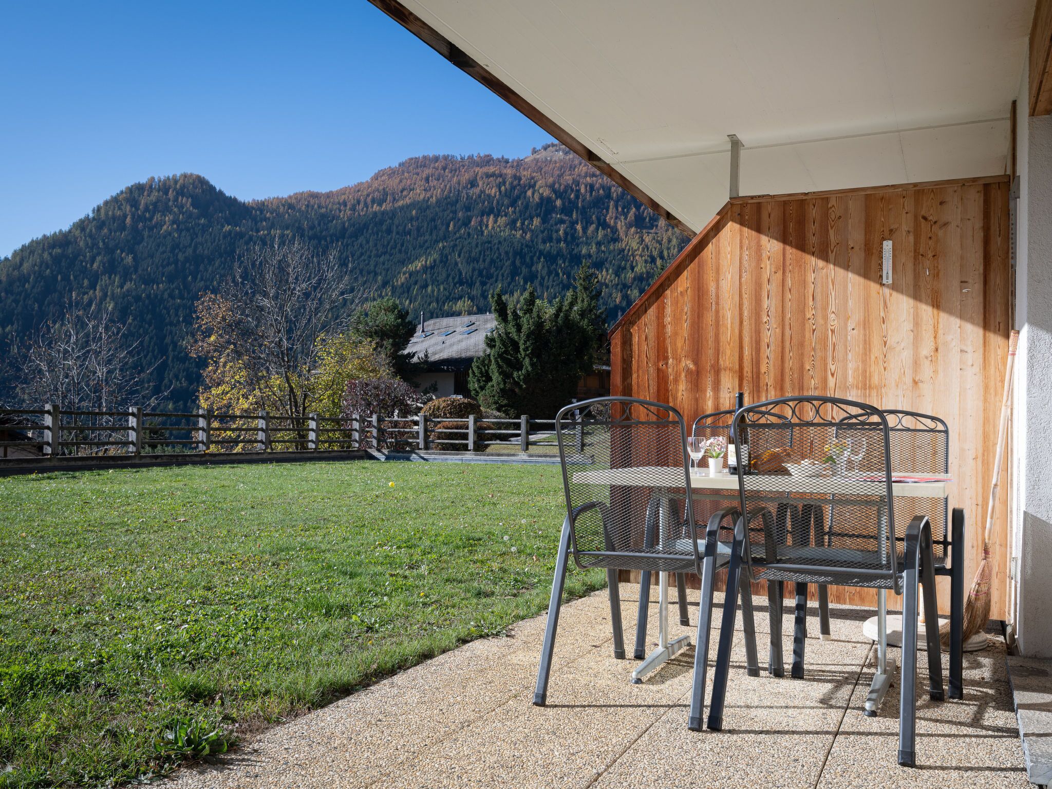 Un patio con mesa y sillas, un edificio de madera y un paisaje montañoso al fondo.