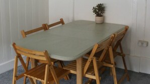 A dining area with a round table and wooden chairs, a potted plant, and shelves with various items. - Dinham Cottage - Cornish Cottage in Boscastle Harbour (Boscastle)