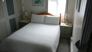 A neatly made bed with white linens, two bedside tables with lamps, and a green nightstand drawer. - Dinham Cottage - Cornish Cottage in Boscastle Harbour (Boscastle)