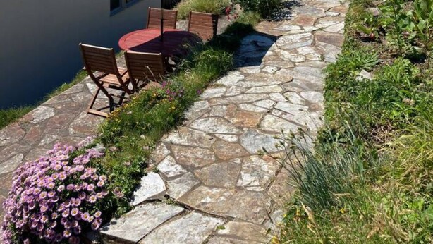 A stone pathway leading to a building with a blue umbrella, outdoor seating, and a flower bed. - Dinham Cottage - Cornish Cottage in Boscastle Harbour (Boscastle)