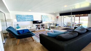 Un saló modern amb un sofà, una cadira, una televisió i una zona de menjador amb taula i cadires.