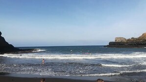 Platja amb onatge, un penya-segat rocos i un cel serè.