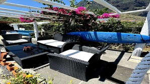 Patio esterno con mobili in vimini, tavolo blu e fiori rosa.
