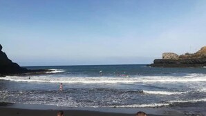 Una spiaggia con onde, una scogliera rocciosa e cielo sereno.