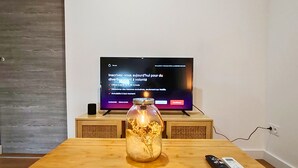 Un tavolo in legno con un barattolo di vetro contenente fiori secchi, un telecomando e un televisore che mostra uno schermo promozionale.